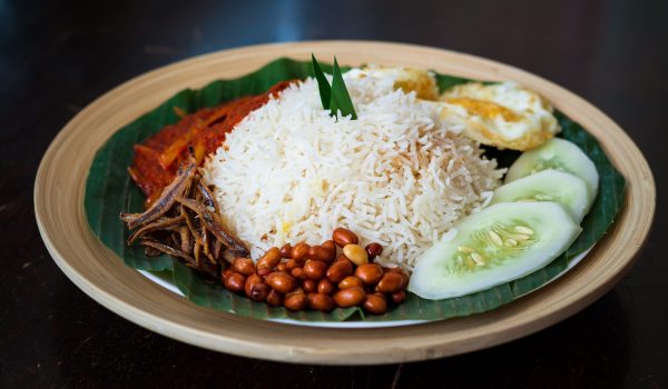 Traditonal Malaysia Asian food Nasi Lemak on a banana leaf in a wooden bamboo plate.