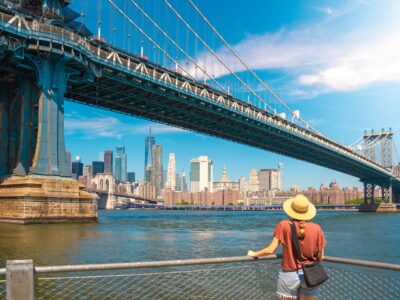 Young woman enjoying view of city skyline in New York. Happy lifestyle girl with hat traveling tourist on bridges. High quality photo