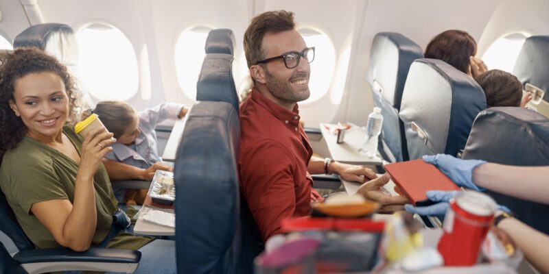 Happy passengers smiling while female flight attendant serving lunch on board. Travel, service, transportation, airplane concept